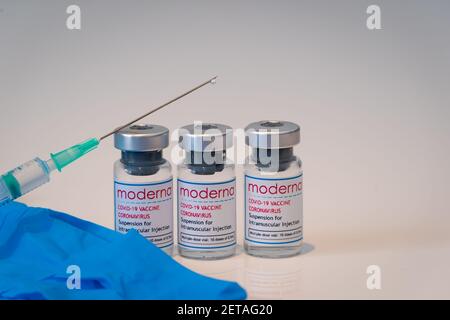 LONDON, ENGLAND - 28. FEBRUAR 2021: Glasfläschchen, die Dosen des Moderna COVID Coronavirus-Impfstoffs mit einer Spritzeninjektion und einem Tröpfchen bei t enthalten Stockfoto