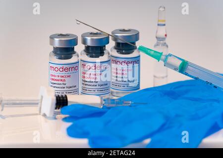 LONDON, ENGLAND - 28. FEBRUAR 2021: Glasfläschchen mit Dosen des Moderna COVID Coronavirus-Impfstoffs mit zwei Spritzen mit einem Tropfen am Knie Stockfoto