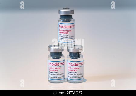 LONDON, ENGLAND - 28. FEBRUAR 2021: Dreieckiger Stapel von drei Glasfläschchen, die Dosen des Moderna COVID Coronavirus COVID-19 Impfstoffs auf Plain enthalten Stockfoto