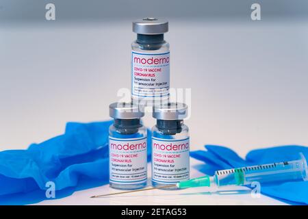 LONDON, ENGLAND - 28. FEBRUAR 2021: Dreieckiger Stapel von drei Glasfläschchen, die Dosen des Moderna COVID Coronavirus COVID-19 Impfstoffs mit Syr Stockfoto