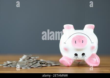 Auf dem Tisch liegen Münzen und ein auf den Kopf stehendes Sparschwein Stockfoto