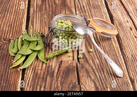 Geschälte Erbsen in einem Glas mit den Schoten auf Die Seite auf einem Holztisch Stockfoto