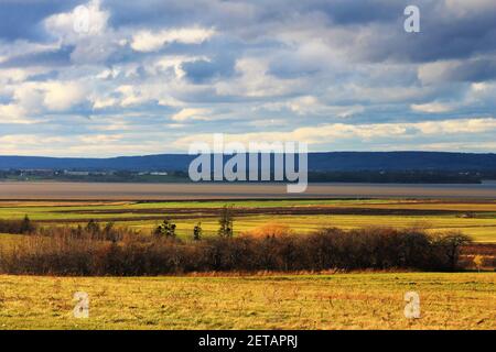 Ein Panoramablick auf Ackerland am Rande einer Bucht von Wasser, mit einer Stadt und Hügel in der Ferne. Stockfoto