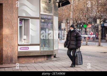 BELGRAD, SERBIEN - 14. FEBRUAR 2021: Mann mit einer Atemschutzmaske, der während des Coronavir in der Straße von Belgrad mit einem Lebensmittelbeutel spazierenging Stockfoto