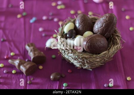 Vogelnest mit Schokoladeneiern, Schokoladenhasen und Süßigkeiten auf dem Tisch Stockfoto