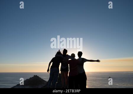 Eine Silhouette von Wanderern am Rande einer Klippe Während Sie den Sonnenaufgang über einem ruhigen Meer genießen Stockfoto