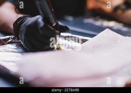Nahaufnahme von Tattoo-Künstler Hand in schwarzen Handschuh Kommissionierung Tinte aus Tintenschale mit einem Tattoo-Stift. Stockfoto
