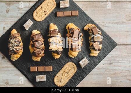 Blick von oben auf gebackene süße Croissants auf dem schwarzen Teller Mit Schokoladenkeks und Sahne auf dem Tisch Stockfoto