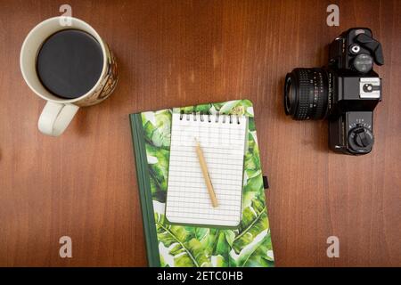 KATOWICE, POLEN - 12. Feb 2021: Draufsicht auf ein Notizbuch, das auf einem Holztisch neben einer Vintage-Kamera und Kaffee liegt Stockfoto