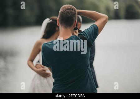 Ein flacher Fokus eines jungen männlichen Fotografen, der fotografiert Eines frisch verheirateten Paares in einem Park Stockfoto