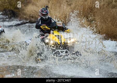 Der Mann auf dem ATV kreuzt einen Stream. Touristischen Spaziergänge auf einem cross-country Gelände. Stockfoto