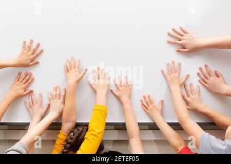 Viele Kinderhände auf dem Hintergrund einer weißen Schultafel. Leerer Platz für die Inschrift Stockfoto