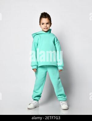 Frolic Kid Boy mit stylischem Haarschnitt in pastellfarbenem, modernem Grün, minzfarbenem Hoodie steht ruhig, leise warten, zuhören Stockfoto