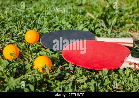 Staubige Tischtennisschläger und orangefarbene Bälle im grünen Gras. Das Konzept der Outdoor-Sportspiele Stockfoto