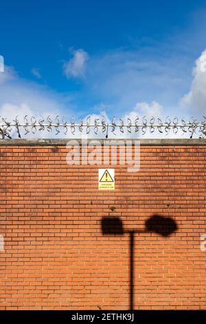 Rote Ziegelwand mit Anti-Diebstahl-Spikes entlang der ganzen Spitze. Stockfoto