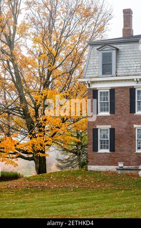 Landschaft mit einem traditionellen viktorianischen Stil alten Backsteinhaus mit Ein Dachboden und ein Kamin und Herbst orange Ahornbaum Am Hang bei nebligen Wetter Stockfoto