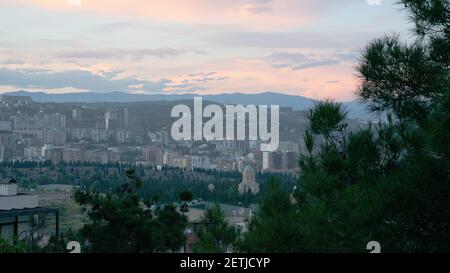 Die Stadt Tiflis, Georgien mit Hügeln und Bergen im Hintergrund durch die grüne Tanne am ruhigen, schönen Abend gesehen Stockfoto