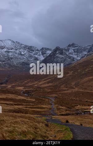 Lange Straße mit verschneiten Bergen, berühmter Sightseeing-Ort, bewölktem Himmel - Fairy Pools - Skye Island - Schottland - Großbritannien Stockfoto