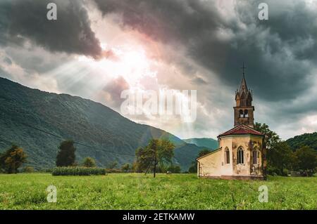 Alte Kirche in den Bergen mit Sonnenstrahlen, die durch den wolkigen Himmel scheinen. Symbol der Hoffnung Stockfoto