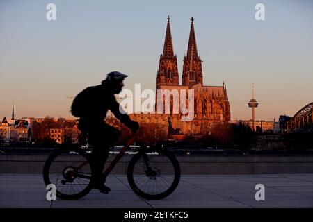 Köln, Deutschland. März 2021, 02nd. Ein Radfahrer fährt am Morgen an der Kathedrale vorbei, beleuchtet von der aufgehenden Sonne. Quelle: Oliver Berg/dpa/Alamy Live News Stockfoto