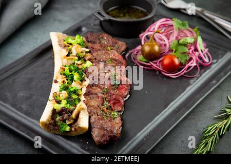 Rindersteak mit Zuckerknochen, serviert mit Sauce und Salat aus Zwiebeln, Pomiloren und Paprika. Dunkler Hintergrund Stockfoto