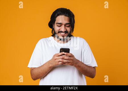 Glücklicher junger indischer Mann mit Handy isoliert über gelb Hintergrund Stockfoto