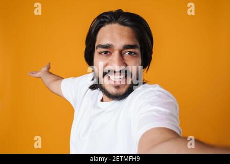 Lächelnder indischer Mann nimmt ein Selfie isoliert über gelben Hintergrund, lässige Kleidung, zeigt Kopieplatz Stockfoto