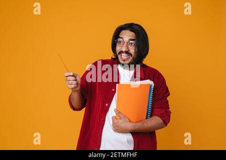 Aufgeregt junge indische Mann Student hält Lehrbücher isoliert über gelb Hintergrund Stockfoto