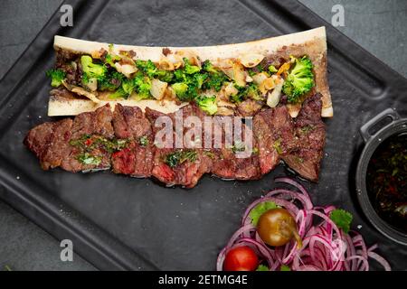 Rindersteak mit Zuckerknochen, serviert mit Sauce und Salat aus Zwiebeln, Pomiloren und Paprika. Dunkler Hintergrund Stockfoto