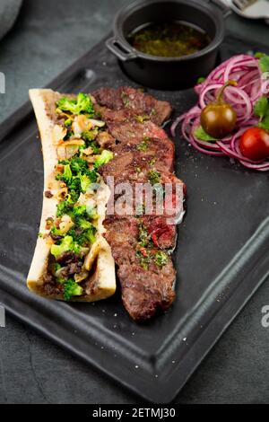 Rindersteak mit Zuckerknochen, serviert mit Sauce und Salat aus Zwiebeln, Pomiloren und Paprika. Dunkler Hintergrund Stockfoto