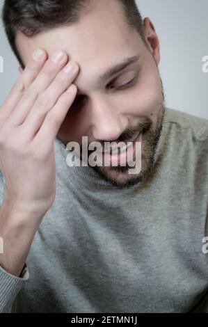 Porträt eines lächelnden jungen Mannes, der seine Stirn berührt Ein Moment der Verlegenheit Stockfoto
