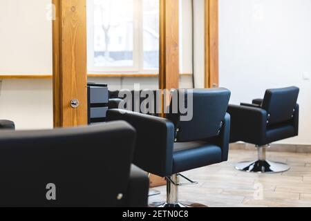 Schönheitssalon Barbershop Interieur. Bequeme schwarze Ledersessel vor großen Panorama-Spiegeln in stilvollen Holzrahmen in einem modernen, gemütlichen Stockfoto