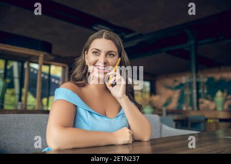 Lächelnde hübsche Frau im Café, die auf dem Smartphone spricht Stockfoto