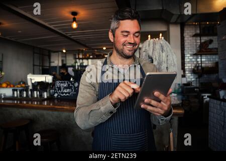 Männlicher Kellner lächelt, während er das monatliche Gehalt auf einem digitalen Tablet erhält Im trendigen Cafe Stockfoto