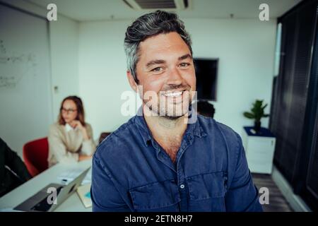 Porträt eines lächelnden kaukasischen Geschäftsmannes, der selbstbewusst steht, während Kollegen arbeiten Im Hintergrund Stockfoto