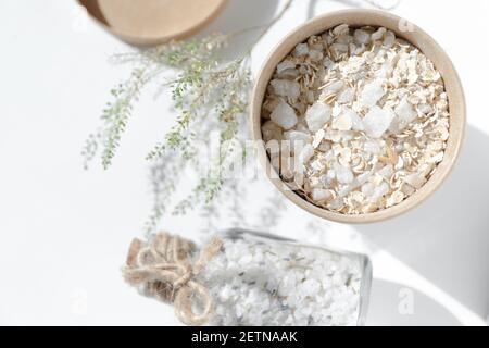 Pappbecher mit Haferflocken und Meersalz. Spa-Produkte zur Reinigung der Haut und für ein entspannendes Bad in einem Glas mit einem Korkstopfen auf einem weißen Stockfoto