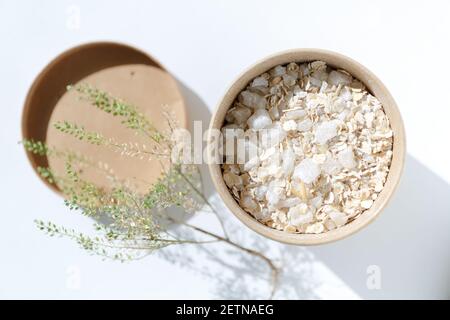 Pappbecher mit Haferflocken und grobem Meersalz aus nächster Nähe. Schrubben Sie die Haut. Spa-Produkte zur Hautreinigung und Entspannungsbad auf weißem Hintergrund mit Stockfoto