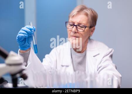 Wissenschaftler Senior Frau Blick in Reagenzglas für biochemische Tests. Doktor in der weißen Mantel Forschung ein neues Experiment im Labor, Analyse der Biotechnologie Arbeit mit modernen Geräten Stockfoto