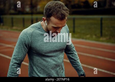 Der kaukasische männliche Sportler spazierengeht mit Ohrhörern auf dem Trackingfeld Stockfoto