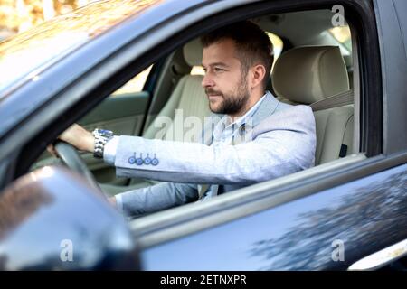 Scharfer gekleideter Mann, der hinter seinem Lenkrad sitzt Automobil Stockfoto