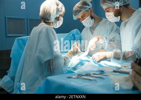 Ein internationales Ärzteteam führt eine komplexe chirurgische Operation an einem unter Anästhesie stehenden Patienten durch. Moderner Operationssaal und erfahrene Chirurgen Stockfoto