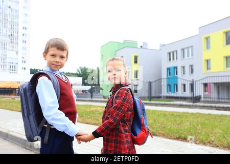 Kinder mit Aktentaschen über den Schultern auf dem Hintergrund der Schule. Stockfoto