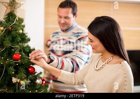 Attraktives Liebespaar schmückt den Weihnachtsbaum für die Feiertage Stockfoto