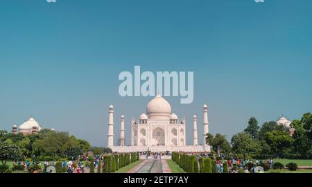 Frontalansicht des schönen Taj Mahal von Bäumen mit grünen Blättern und ein paar Besucher an einem hellen Sommermorgen in Agra, Indien flankiert. Stockfoto