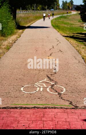 Start einer Radstraße neben einem Park, mit einem Schild auf dem Boden gemalt, mit einigen Radfahrern im Hintergrund aus Fokus Stockfoto