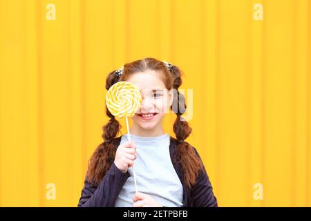 Mädchen mit einem großen Süßigkeiten in den Händen auf einem gelben Hintergrund. Stockfoto