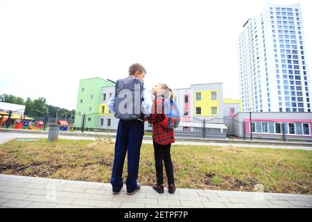 Kinder mit Aktentaschen über den Schultern auf dem Hintergrund der Schule. Stockfoto