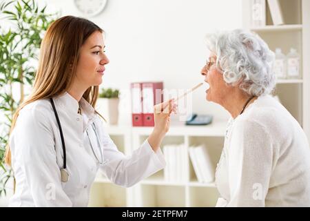 Schöne junge Arzt untersucht Hals zu alten älteren Frau Stockfoto