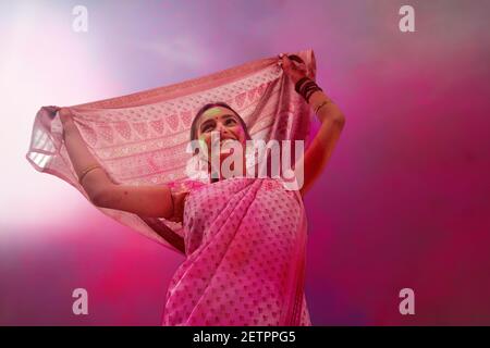 EINE JUNGE FRAU TRÄGT SAREE GLÜCKLICH POSIERT MIT FARBEN ALLE ÜBER SIE Stockfoto
