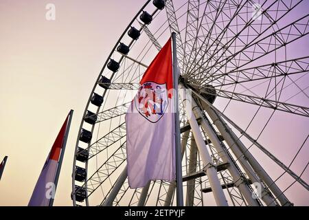 Riesenrad bei Sonnenuntergang in der Düsseldorfer Altstadt mit Fahne von Nordrhein-Westfalen vorne. Stockfoto